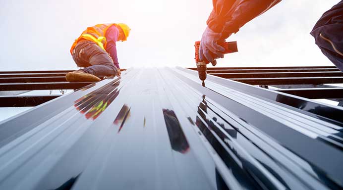 Roofer installing long run metal roofing on a commercial building